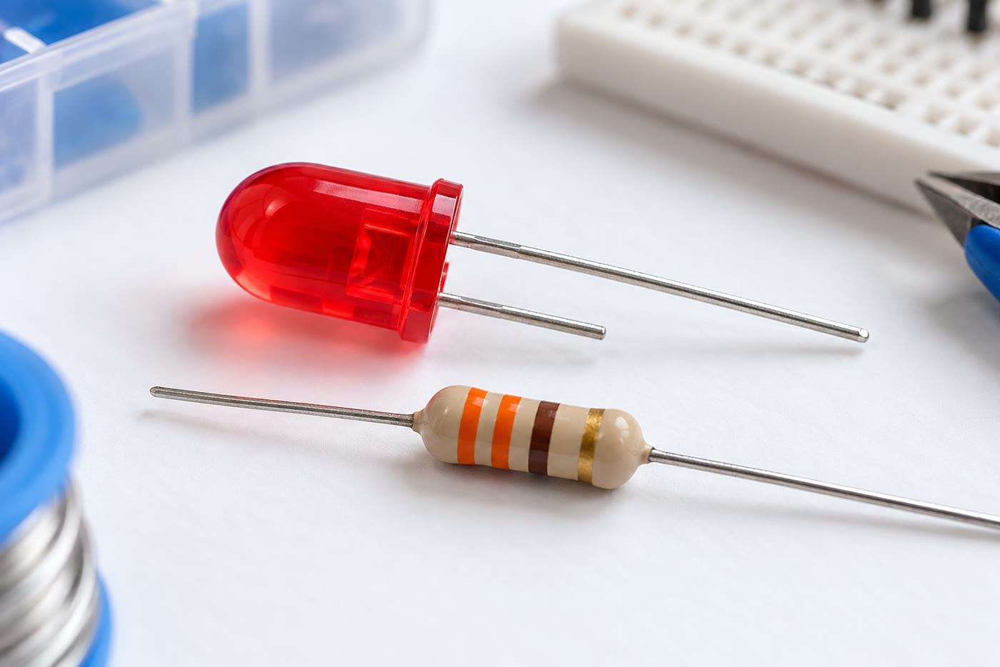 LED rojo de 5 mm con una pata larga y una corta, junto a una resistencia con bandas naranja, naranja, marrón y dorado.